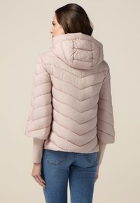 Lyserød pufferjakke med chevron-quilting, hætte og cropped ærmer, parret med blå jeans. Glat tekstur, blød finish.
