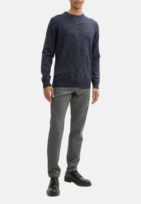 Pull en maille texturée bleu marine avec col rond, associé à un pantalon gris ajusté et des chaussures noires à lacets, créant un look décontracté équilibré.