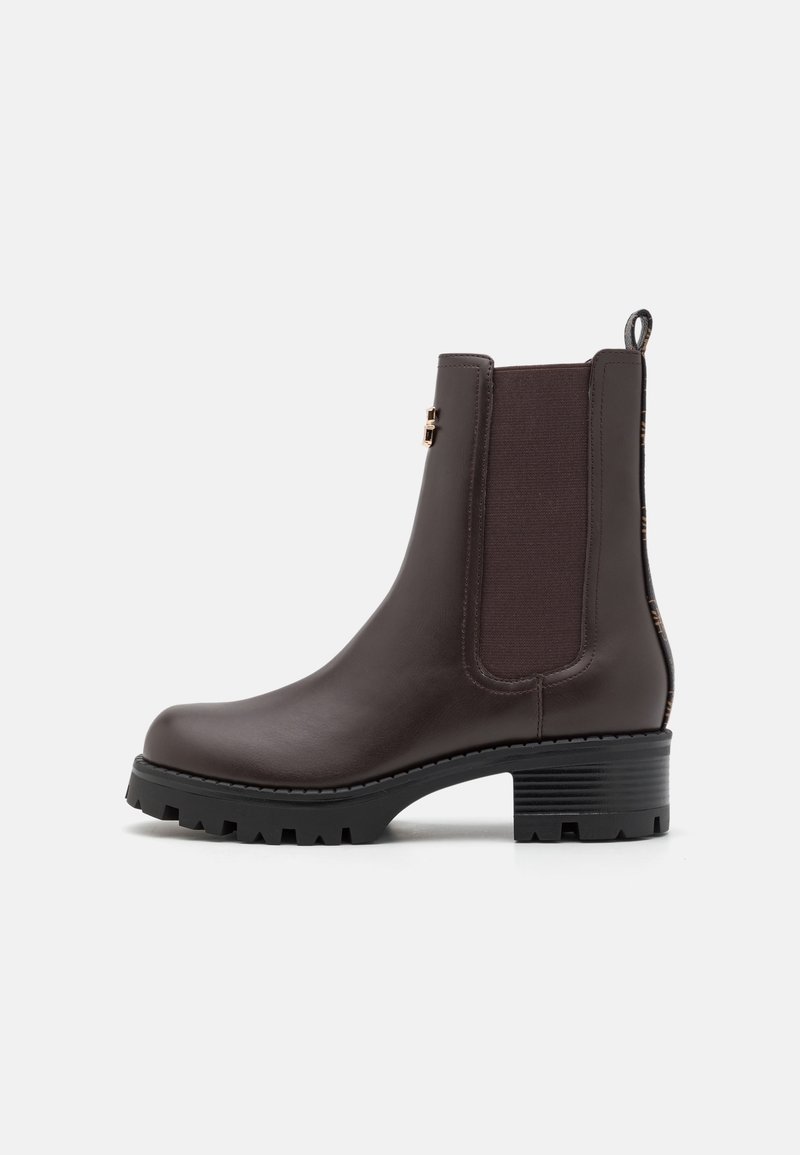 Brown leather ankle boot with elastic side panels, textured back, and a thick, treaded rubber sole. Features a pull tab for easy wearing.