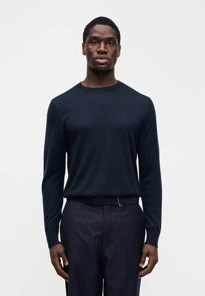 Μπλε σκούρο πουλόβερ με μακριά μανίκια, στρογγυλή λαιμόκοψη και διακριτική λεπτομέρεια με λογότυπο, συνδυασμένο με μπλε σκούρο παντελόνι με λεπτές ρίγες. Μαλακό υφαντό ύφασμα, εφαρμοστό στυλ.