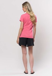 Ružové tričko s krátkym rukávom a okrúhlym výstrihom, kombinované s čiernymi šortkami. Tkanina pôsobí mäkko a hladko, vhodná na bežné nosenie.