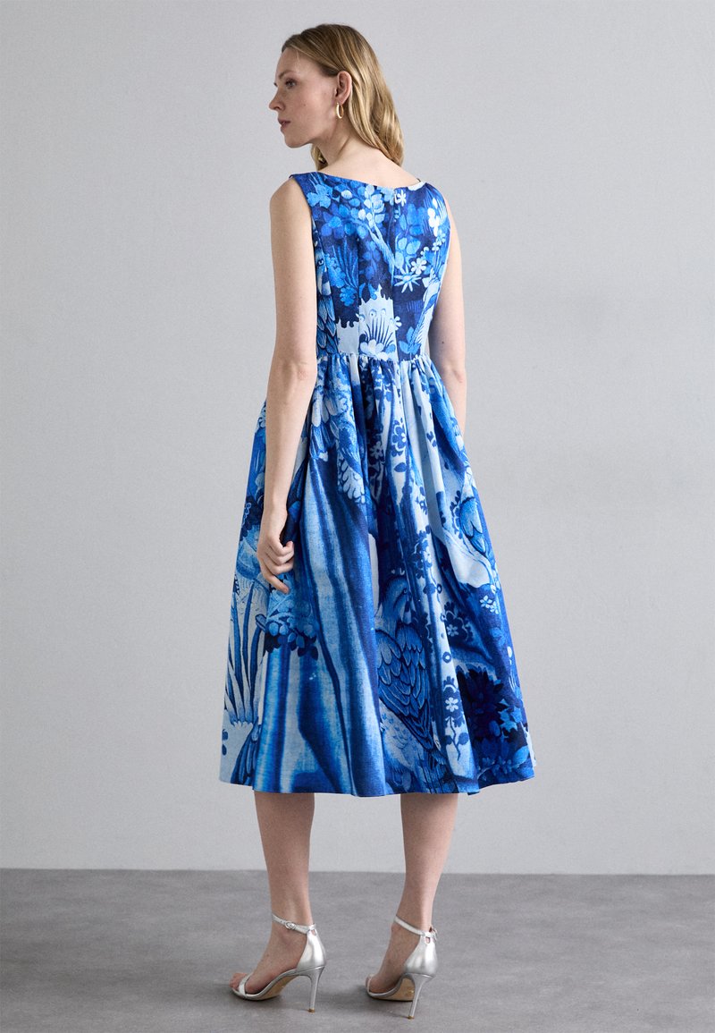 Abito floreale blu con un corpetto attillato e gonna svasata, caratterizzato da diverse tonalità di blu. Tacchi alti in satin argentato completano il look.