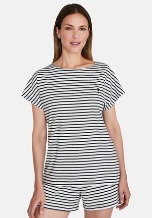 Kvinde iført sort og hvidt, vandret striped kortærmet top og matchende shorts, stående mod en ensfarvet lys baggrund.