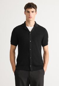 Zwarte kortemouwen knoopshirt met een textuur brei ontwerp, een notch-kraag en een ribgebreide zoom. Eenvoudige en moderne constructie.