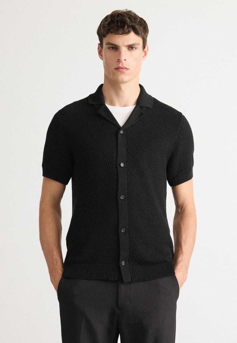 Zwarte kortemouwen knoopshirt met een textuur brei ontwerp, een notch-kraag en een ribgebreide zoom. Eenvoudige en moderne constructie.