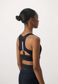 Black sports bra features a racerback design with mesh accents and "STRONGER" text. Paired with high-waisted black leggings with dot details.