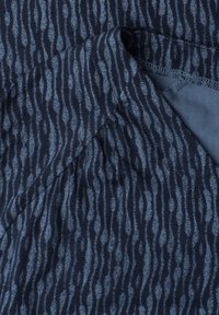 Close-up of dark blue fabric with a wavy vertical pattern in lighter blue, showing folded corner and stitched edge.