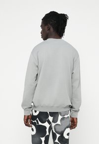 Sudadera gris con cuello redondo y mangas largas, con puños y dobladillo acanalados. Lleva puestas pantalones de patrón floral en blanco y negro.