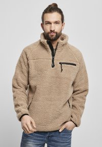 Beige fleece pullover med høj krave, halv lynlås foran og en lynlåslomme på brystet. Blød tekstur med en afslappet pasform.