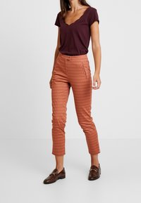 Burgundy short-sleeve top with a scalloped neckline paired with rust-colored patterned trousers featuring a slim fit and side pockets.