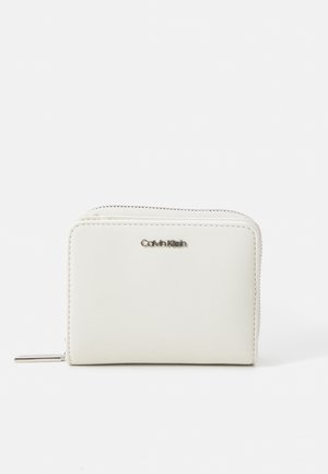 Portafoglio in pelle bianca con una texture liscia, chiusura con zip e logo Calvin Klein in argento sulla parte anteriore. Forma rettangolare compatta.