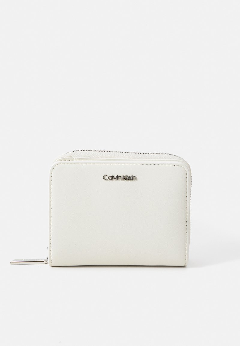 Portafoglio in pelle bianca con una texture liscia, chiusura con zip e logo Calvin Klein in argento sulla parte anteriore. Forma rettangolare compatta.