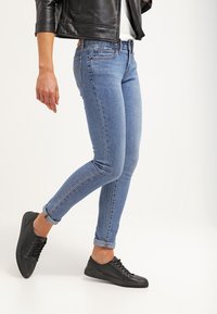 Vaqueros ajustados de un lavado claro en denim con una textura suave, con detalles de costura y dobladillos enrollados, combinados con zapatillas negras de caña baja.