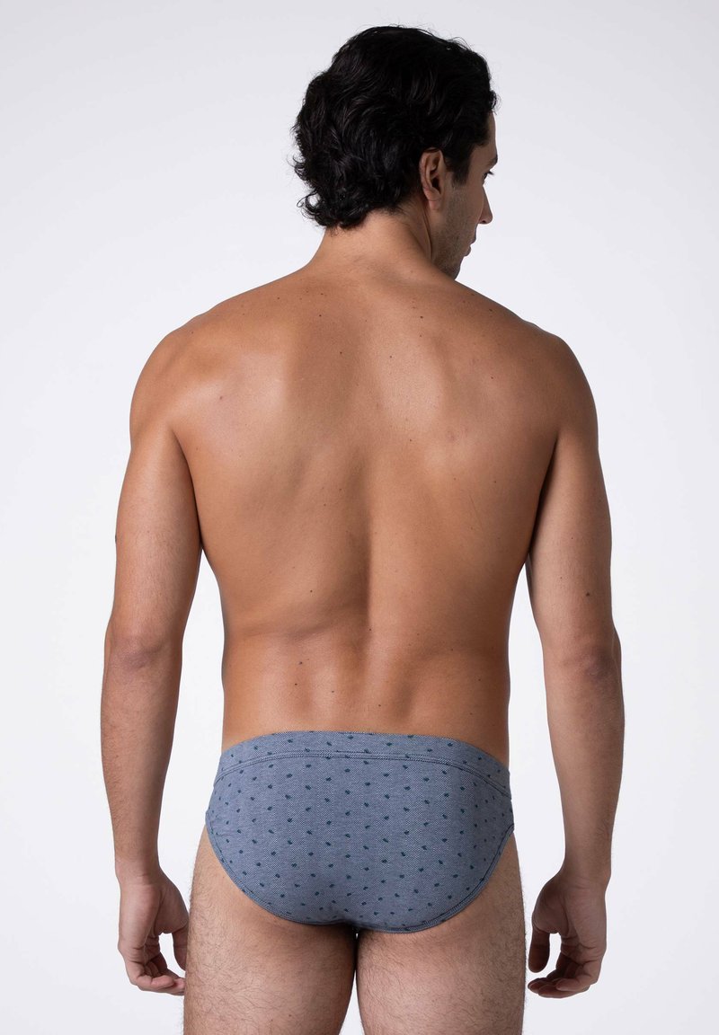 Slip da bagno grigi con motivo a pois, caratterizzati da una vestibilità aderente e un tessuto liscio, mostrati di spalle su un modello.