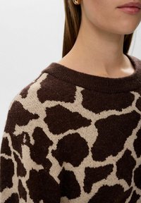 Pull marron et beige avec un imprimé girafe, fabriqué en tissu texturé, présentant un col large et un détail de col côtelé.