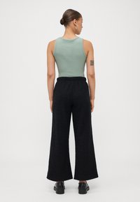 Lysegrønn ribbet tanktop kombinert med svarte vide strukturerte bukser og svarte sko, som viser en avslappet passform og elastisk midje.