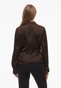 Brown satin blouse with a collar, long sleeves, and buttoned cuffs. Tailored fit with a smooth texture and a slightly curved hem at the back.
