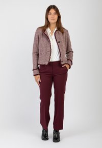 Giacca in tweed bordeaux con orli sfrangiati, due bottoni, indossata sopra una camicia bianca e pantaloni bordeaux, abbinata a stivaletti neri alla caviglia.