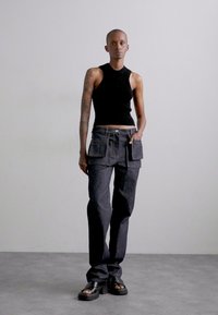 Top negru fără mâneci din material texturat, asociat cu pantaloni cargo închiși la culoare, cu buzunare frontale și o croială lejeră, completat de sandale cu talpă chunky.