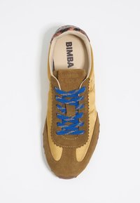 Sneaker in suede marrone con lacci blu, soletta crema etichettata "BIMBA Y LOLA" e suola in gomma marrone texturizzata. Accentuata da un tallone decorato.