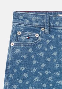 Denim o jasnoniebieskim wzorze kwiatowym, z małą kieszonką z przodu, metalowymi guzikami i kontrastującymi detalami w szyciu.