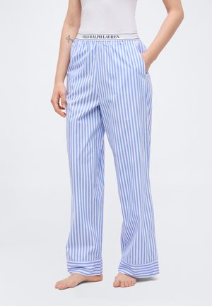 Persoon die blauw-wit gestreepte pyjamabroek met verticale strepen draagt, voorzien van een Polo Ralph Lauren tailleband, met één hand in de zak.