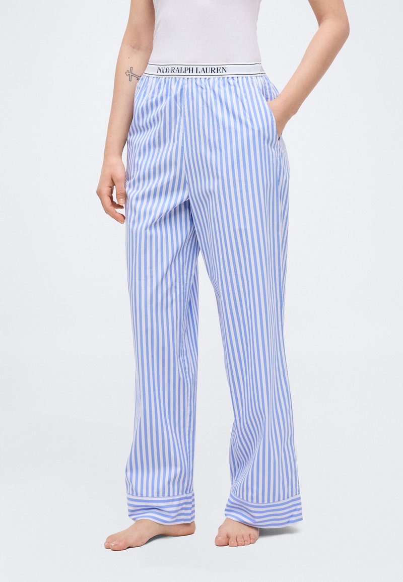 Άτομο που φοράει πυτζάμες με κάθετες ρίγες σε μπλε και λευκό χρώμα, με ζωνάρι Polo Ralph Lauren, και έχει το ένα χέρι στην τσέπη.
