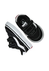 Zapatillas de lona negras con costuras blancas y un diseño clásico de Vans. Cuentan con dos correas de velcro y una suela de goma blanca con detalles rojos.