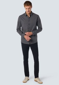 Hemdkraag in marineblauw met een geometrisch patroon in contrasterend wit. Gecombineerd met zwarte broeken en lichte sneakers.