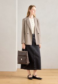 Blazer en pied-de-poule marron, chemisier blanc à boutons, jupe en denim noire, ballerines noires, portant un sac à main marron foncé avec un fermoir doré.