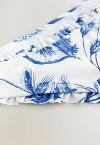 Costum de baie alb, cu un model floral albastru, având o textură strânsă pe talie și un accent delicat de dantelă pe margine.