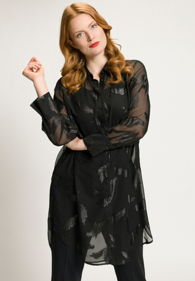 Zwarte doorzichtige blouse met een knoopsluiting aan de voorkant, voorzien van getextureerde zilveren patronen. Lange mouwen en een ronde zoom ronden het ontwerp af.