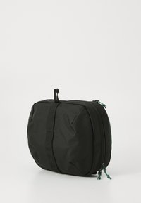 Bolsa negra de nailon con forma rectangular, que cuenta con un asa en la parte superior, cierre de cremallera y una superficie texturizada con una correa para facilitar su transporte.