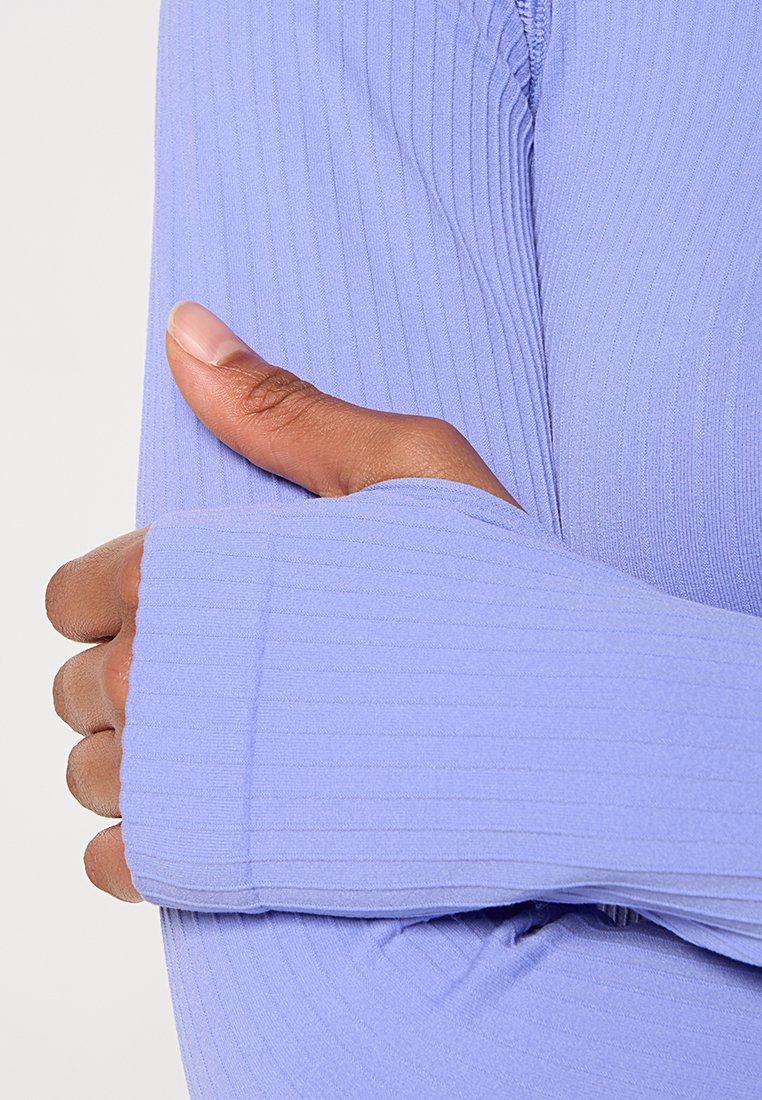 Langärmliges Oberteil in hellem Lavendel, aus geripptem Stoff, mit breiten Bündchen und strukturiertem Finish. Nahaufnahme einer Hand, die auf dem Ärmel ruht.