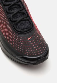 Gros plan sur l'avant d'une basket Nike noire et rouge avec tissu en mesh, lacets et petit logo Swoosh sur le dessus.