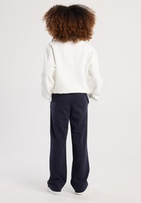 Felpa bianca con vestibilità comoda e polsini a costine abbinata a pantaloni a gamba larga blu scuro. Le sneakers completano l'outfit.