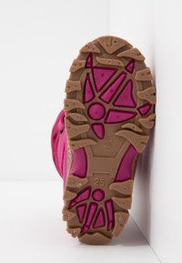 Suela de una bota infantil en tonos rosa y marrón, que muestra surcos profundos y el número de talla 25 sobre un fondo blanco.
