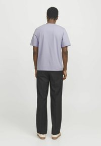 Camiseta corta de manga corta en un suave tono púrpura claro con un ajuste relajado, combinada con pantalones negros y calzado beige. Diseño sencillo, tela suave.