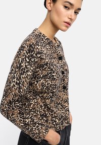 Kardigan w leoparda w brązowym, beżowym i czarnym kolorze. Posiada okrągły dekolt i cztery czarne guziki, wykonany z teksturowanej tkaniny.