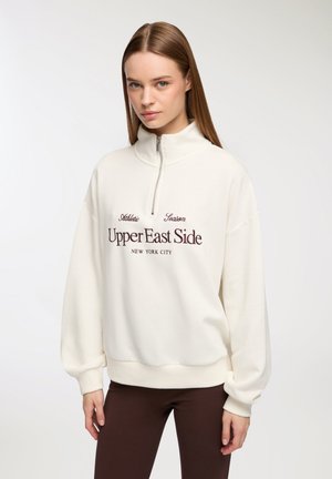 Felpa bianca con colletto alto, mezza zip e polsini a coste. Presenta la scritta ricamata in bordeaux "Upper East Side, New York City."