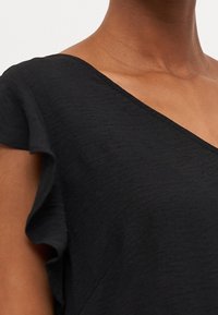 Svart topp med v-ringning och volangärmar. Tillverkad av lätt tyg med en något texturerad yta.