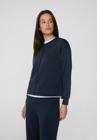 Granatowy sweatshirt z długimi rękawami, okrągłym dekoltem i gładką teksturą. Posiada luźny krój oraz subtelne detale w szyciu.