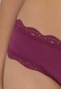 Bordowa bielizna ozdobiona koronką z gładkiego, miękkiego materiału. Koronka ma kwiatowy wzór, co nadaje delikatny wygląd wzdłuż pasa.