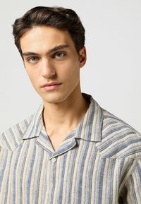 Gestreept shirt van lichte stof in beige en blauwe tinten, met een camp collar en een enkele knoopsluiting. Geweven gestreept patroon.