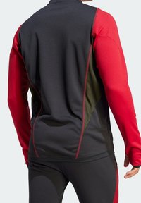 Camiseta atlética de manga larga negra y roja con un diseño ajustado, que presenta costuras en contraste y paneles texturizados en los laterales.