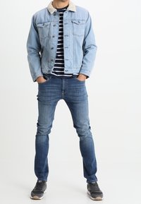 Vaaleansininen farkkutakki, jossa on beige lampaanvillakaulus, päällä musta-valkoraitainen paita. Tummansiniset farkut ja harmaat lenkkarit täydentävät asun.