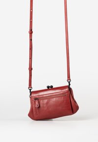 Red leather crossbody bag with a smooth texture, a zippered front pocket, and two rounded bead accents. Adjustable strap attached.