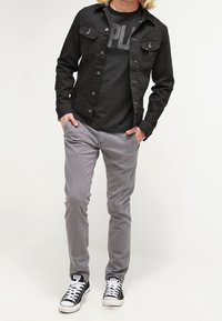 Black denim jacket, gray t-shirt with large print, light gray pants, and black sneakers with white laces. Outfit features a casual design.