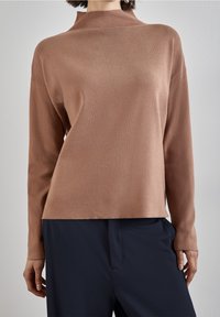Brun stickad tröja med hög krage, långa ärmar och avslappnad passform. Slät textur och minimalistisk design. Matchad med mörka byxor.