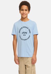 Camiseta de algodón azul claro de manga corta con cuello redondo, que presenta un texto gráfico negro en un diseño circular. Combinada con pantalones cargo beige.